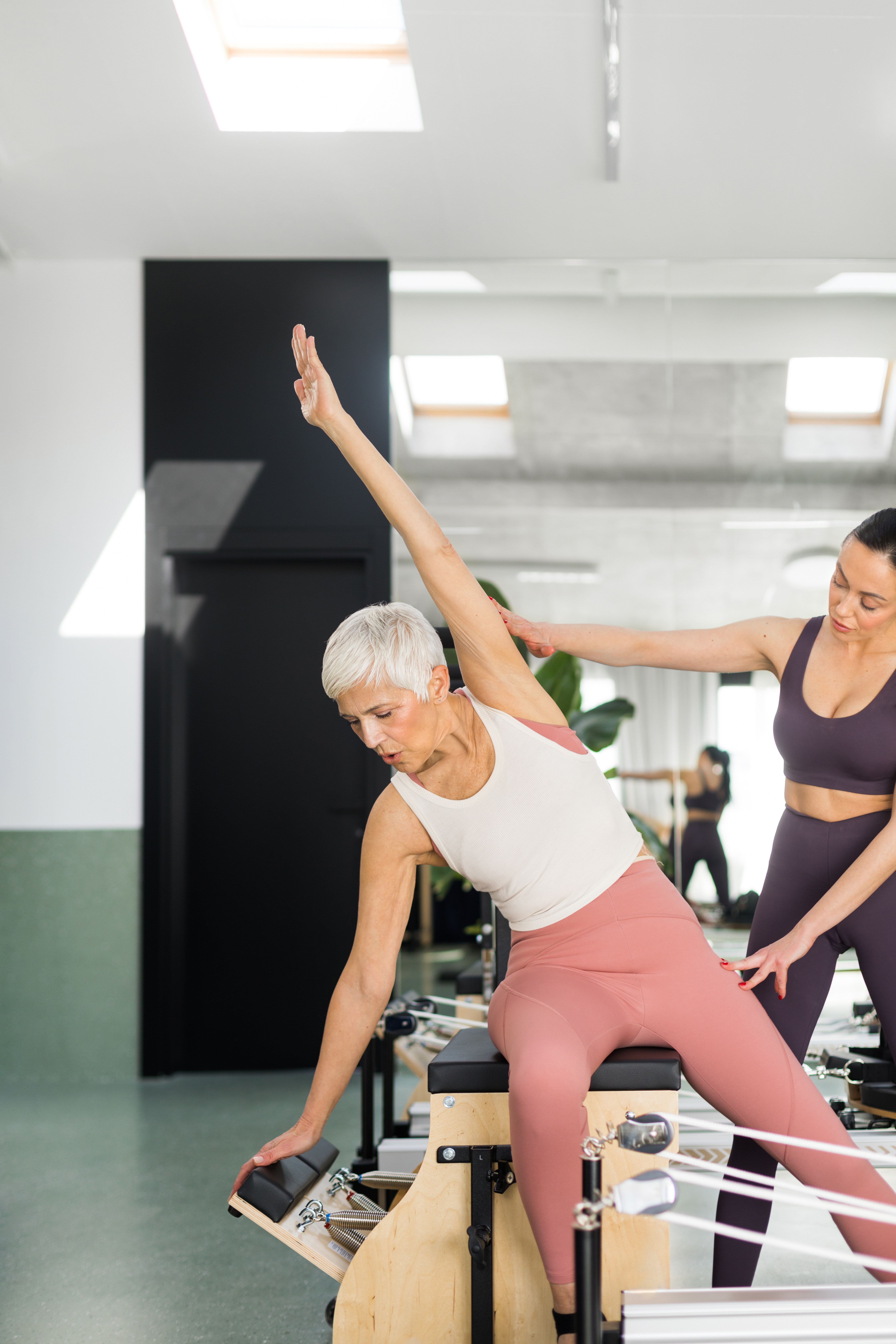 Beautiful senior woman having pilates class on performer machine with instructor