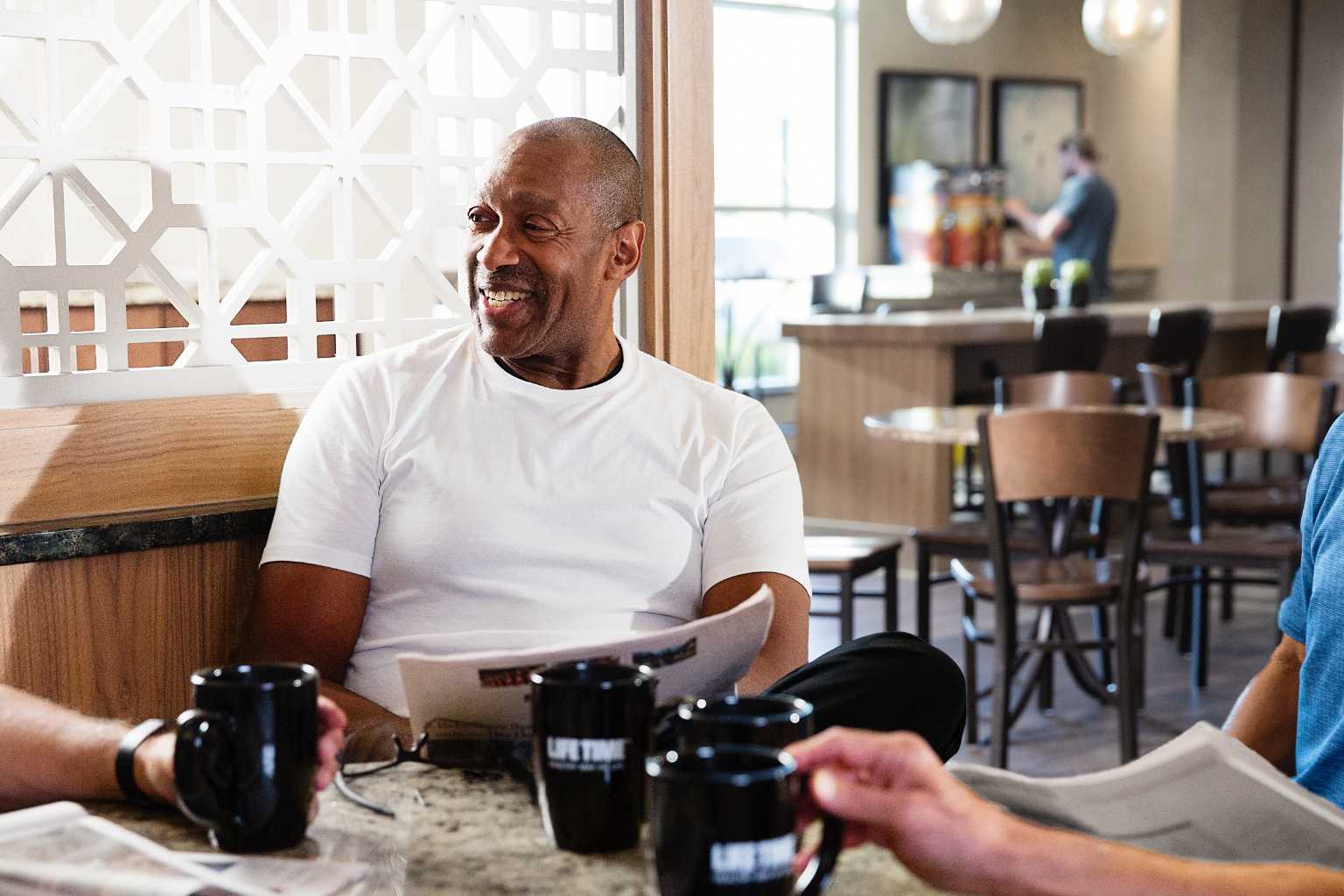 Man sitting in a Life Café with other people, each holding a coffee cup. 