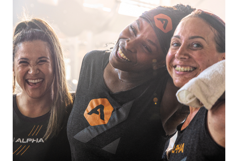 A waist-up shot of three women standing side by side with their arms around each other.