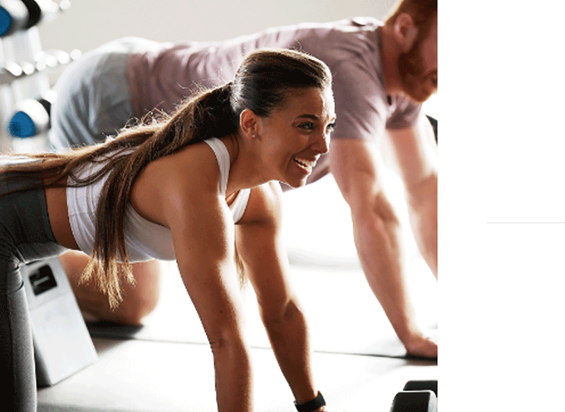 A woman on all fours in tabletop position looks up smiling during a class break. 