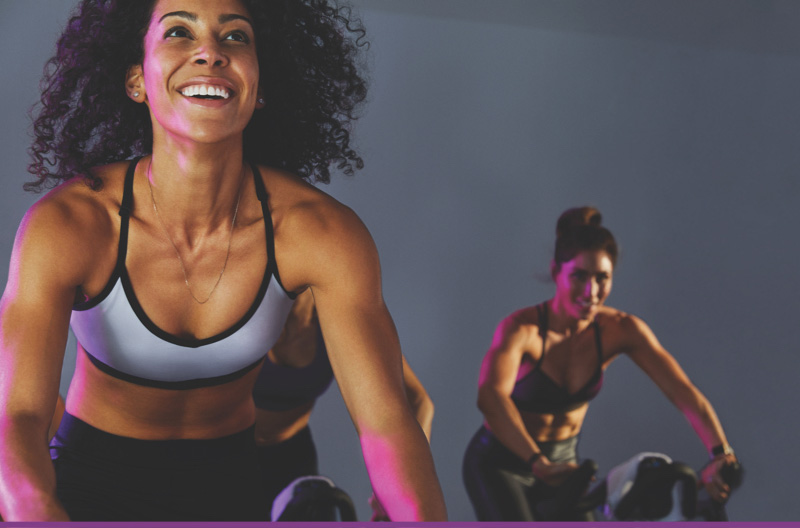 Two women riding stationary bikes in a cycle class